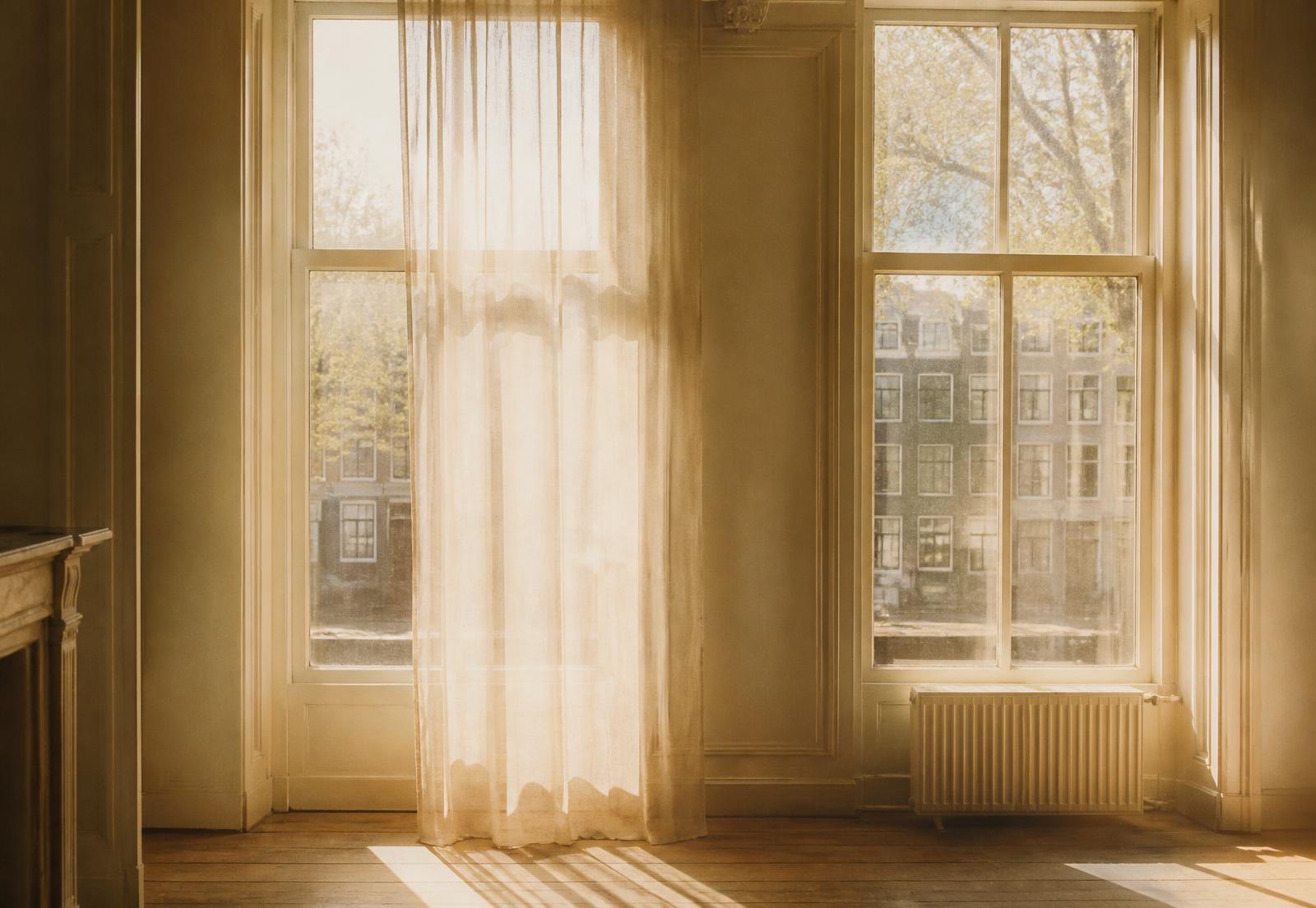 Höga kanalhusfönster i Amsterdam med linnegardin som silar eftermiddagsljus